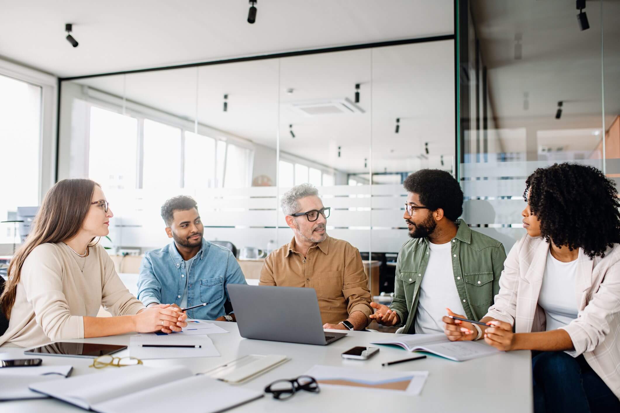 Four professionals discussing work around a laptop in a bright office.