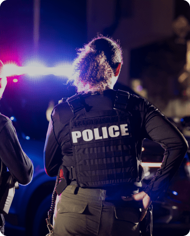 Police officers standing near flashing patrol car lights at night.