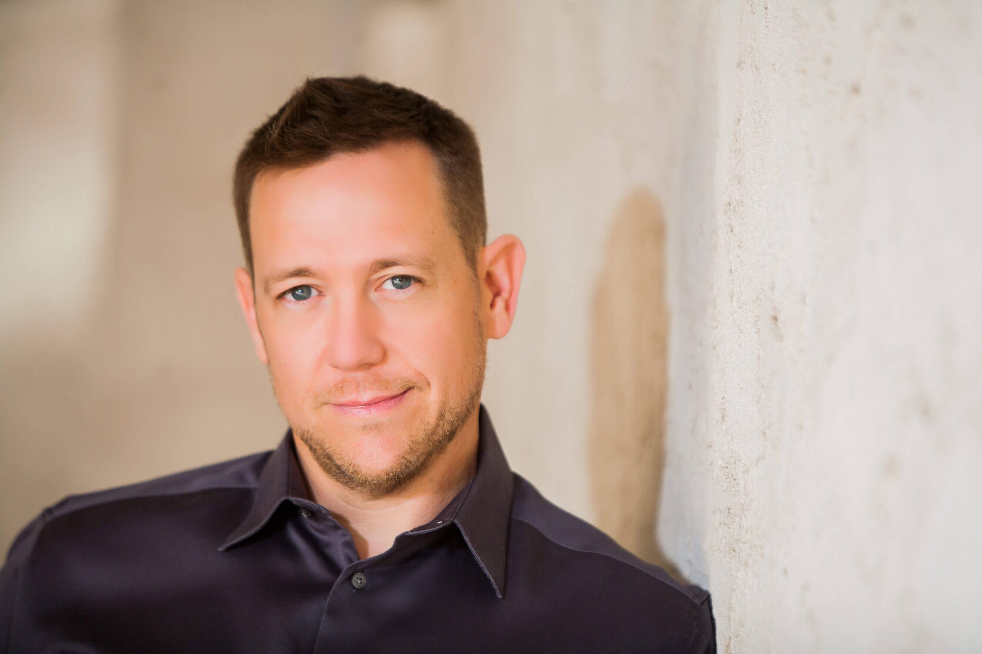 Confident man with short hair and a slight smile against a neutral background.