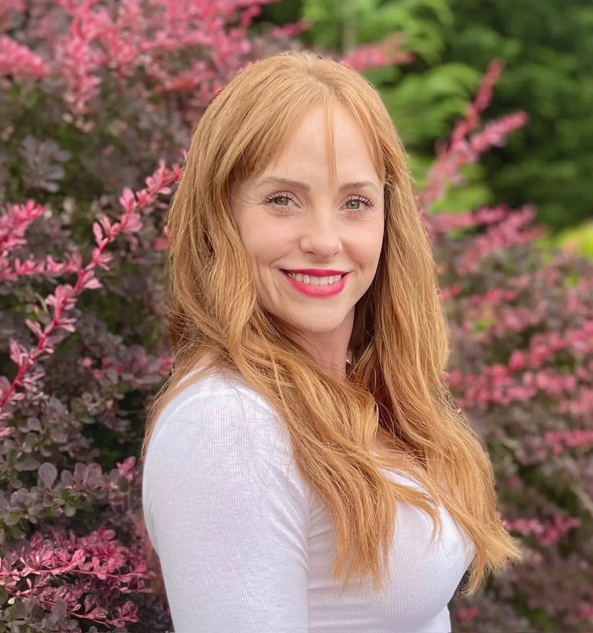 Smiling woman with long hair by bushes.